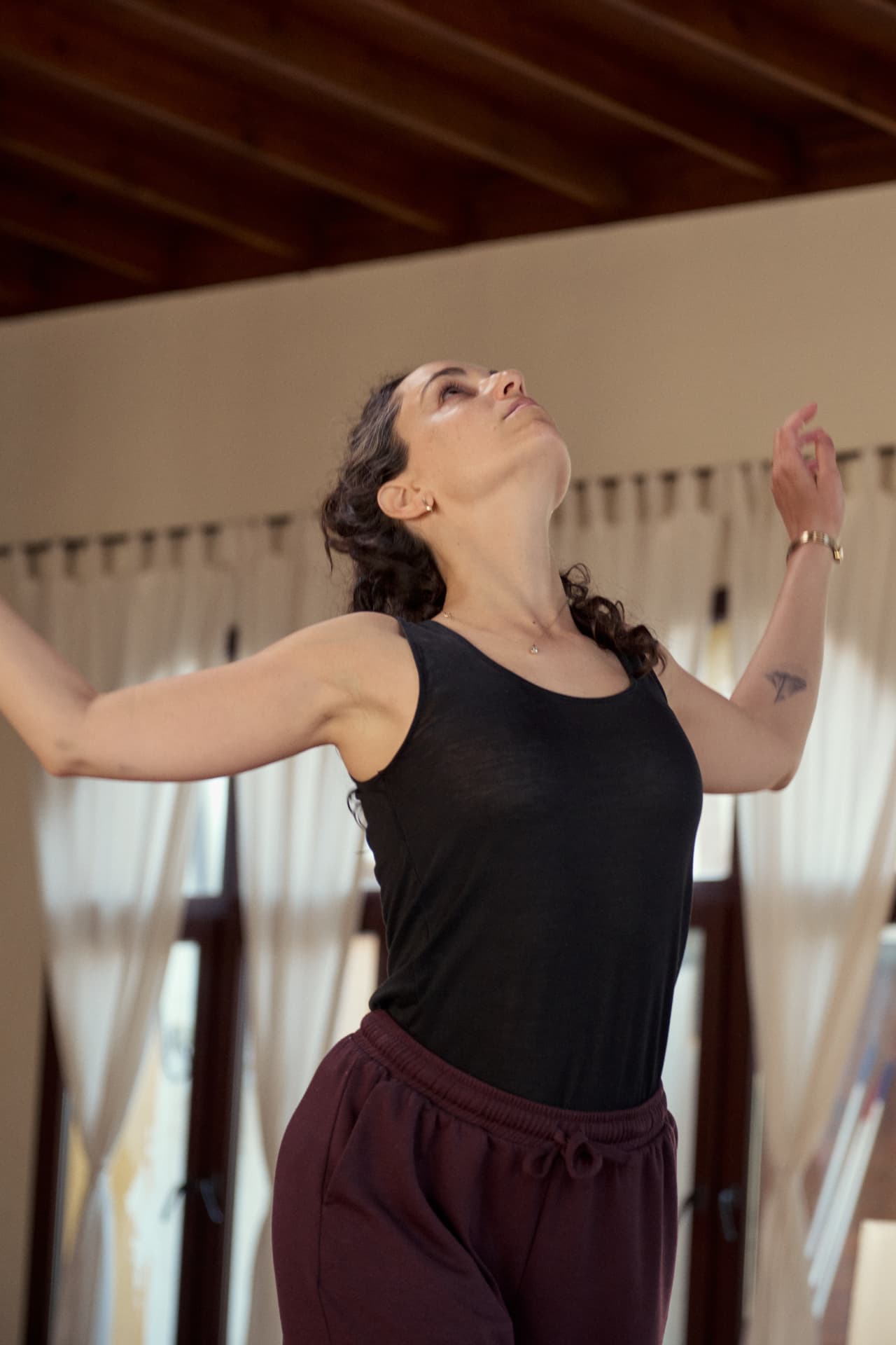 Roni mid-movement with arms open and head lifted in a sunlit studio